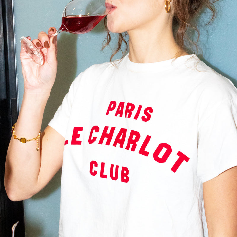 Woman drinking red wine and wearing a white t-shirt with red text.